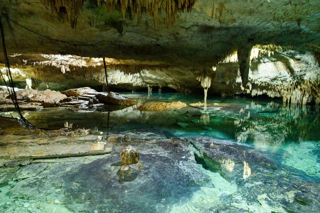 A breathtaking view of a cave with stalactites hanging from the ceiling and clear water reflecting the rock formations below.
