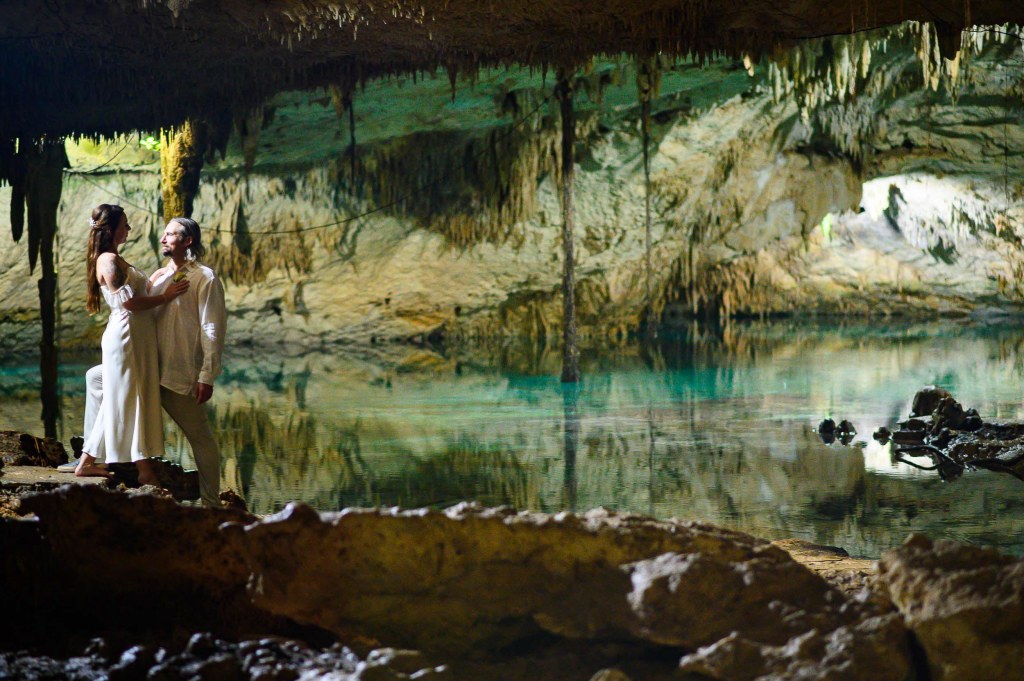 A couple embraces in a cave with stunning rock formations and a clear underground lake.